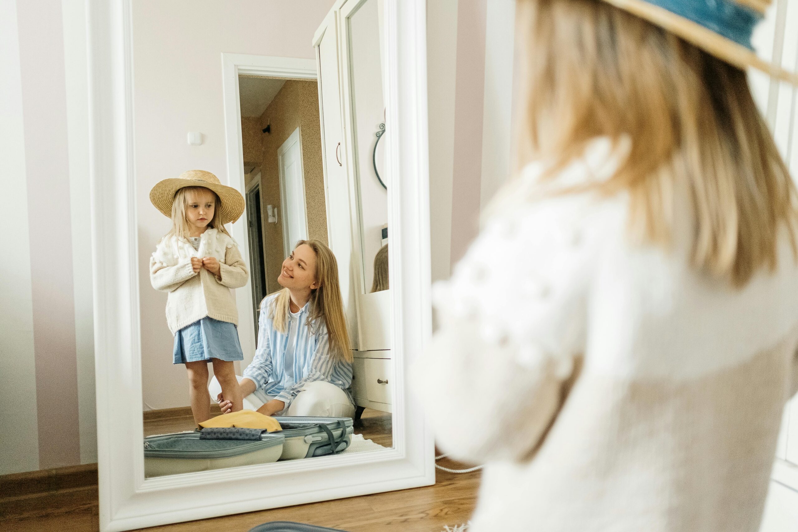 A mother and young daughter share a joyful moment dressing up indoors.