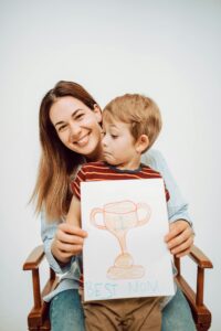 Mother and son smiling with 'Best Mom' drawing on bond paper.