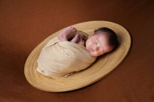Adorable newborn baby peacefully sleeping in a woven basket on brown background.