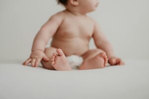 Adorable baby sitting and playing indoors, showcasing innocence and softness.