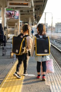 Children with school bags walking on a sunny train station platform, exploring.