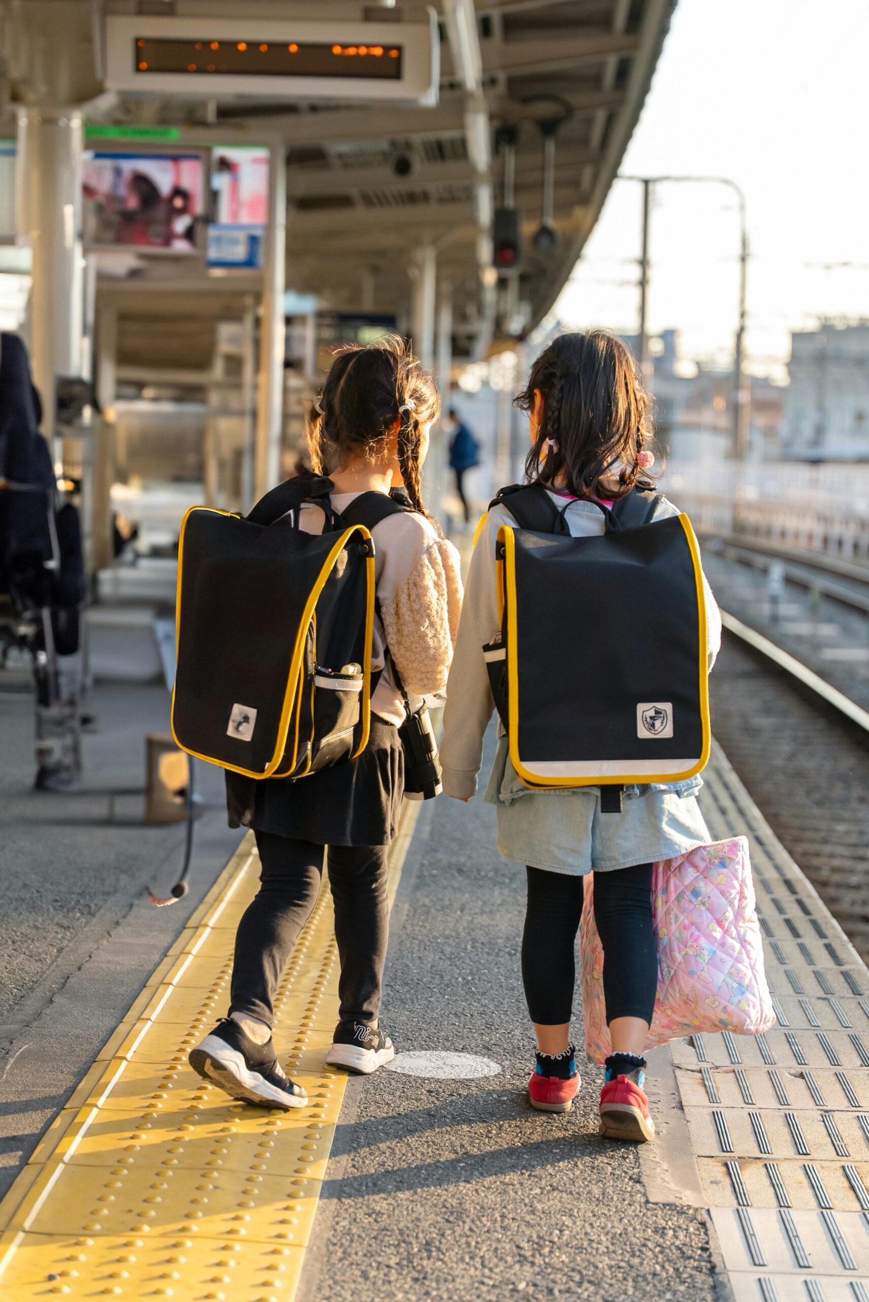 Children with school bags walking on a sunny train station platform, exploring.