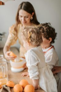 Family making fresh orange juice together in the kitchen, modeling healthy eating habits for kids.
