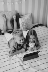 Two children watching a tablet on bed with a teddy bear, representing balanced screen time in digital parenting.