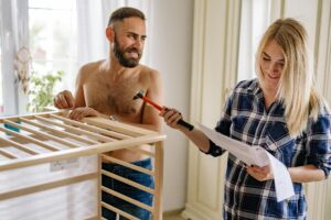 A man and woman assembling a crib together with tools and instructions.