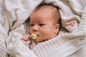 Close-up of an adorable baby with a pacifier wrapped in a cozy blanket.