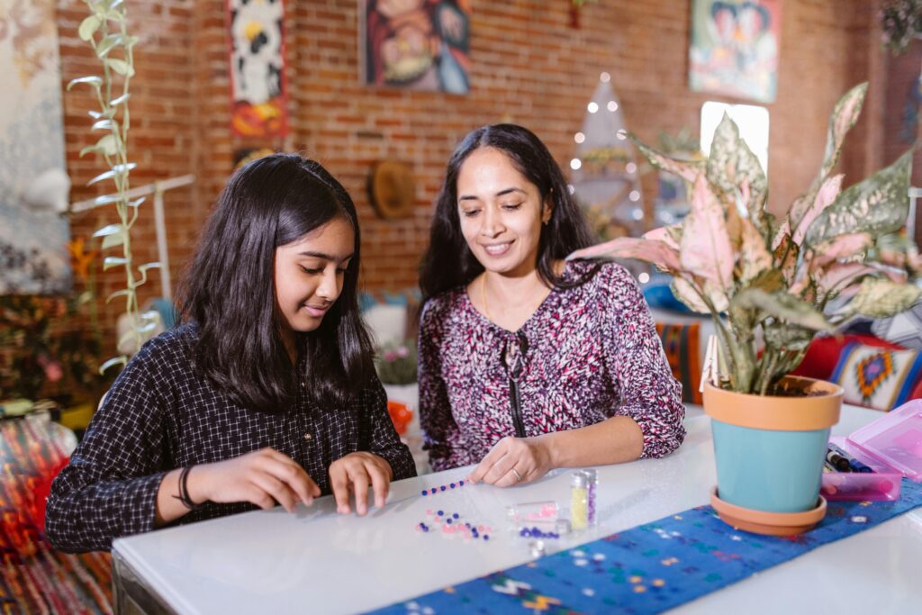Mother and daughter creating a colorful beaded bracelet together at home. Parenting teenagers in 2025.